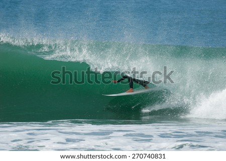 A surfer in a wetsuit rides a tube on a beautiful ocean wave.