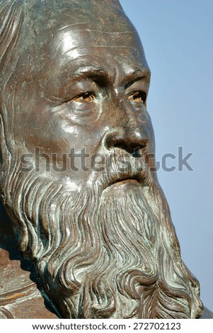 An old and aged bronze bust or statue of a man\'s face with a long beard.