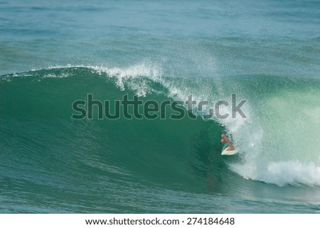 A surfer rides inside the tube of a beautiful green ocean wave.