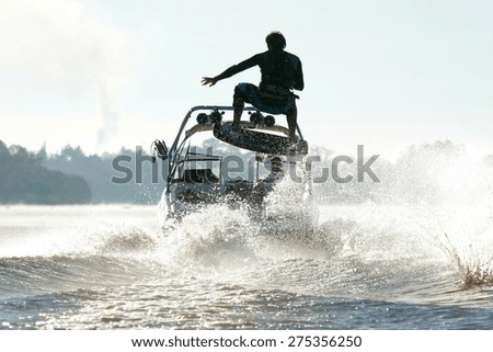 Silhouette of a wake skater as he launches off the wake behind a boat.
