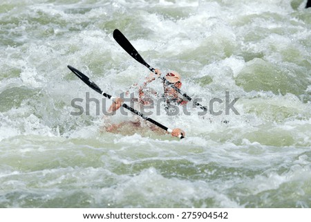 A K2 canoe with two paddlers is completely submerged as it navigates a wild rapid in a river.