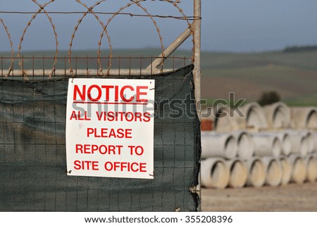 A sign on the fence of a construction site instructs visitors to report to the site office.
