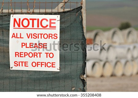 A sign on the fence of a construction site instructs visitors to report to the site office.