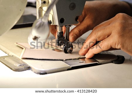 Closeup of a woman's hands as she operates an industrial sewing machine in a shoe factory, hand-stitching a the leather upper of a shoe. Shallow depth of field.