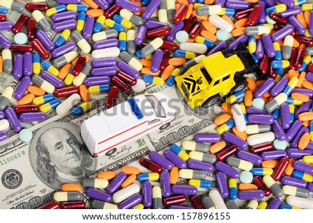 Bulldozer clears the way for the ambulance through the dollars, pills and tablets (installation on the theme of modern medicine trends)