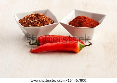 Red milled and flaked chili pepper in white bowl and bean pods