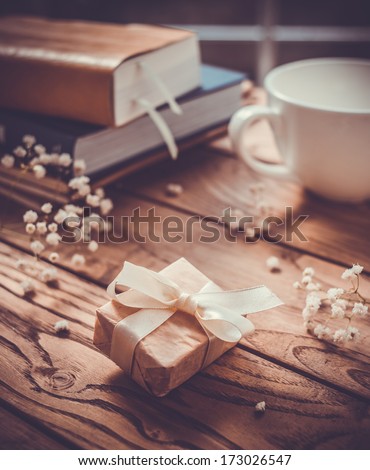 Books, flowers, white cup and wrapped gift box on wooden table. Toned picture