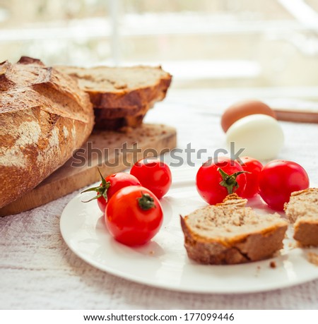 Bread, boiled eggs and cherry tomatoes on white table