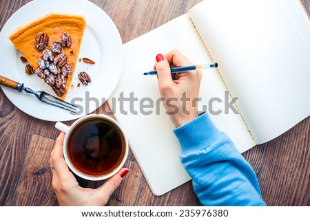 Woman hands drawing or writing, tea, pumpkin cake on wooden table. Toned picture