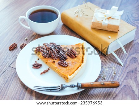 Pecan and pumpkin cake on plate with tea and books on wooden background. Toned picture