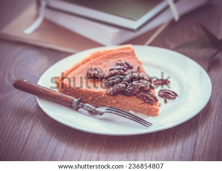 Pecan and pumpkin cake on plate with books on wooden background. Toned picture