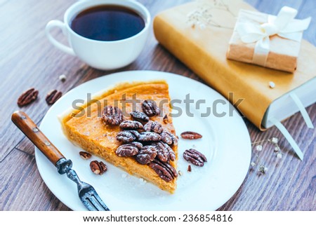 Pecan and pumpkin cake on plate with tea and books on wooden background. Toned picture
