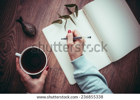 Woman hands drawing or writing in open notebook on wooden table. Toned picture