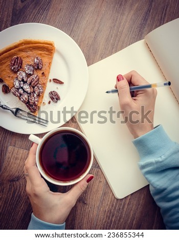 Woman hands drawing or writing, tea, pumpkin cake on wooden table. Toned picture