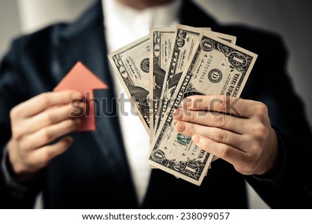 Business person holds dollar bills and red arrow.  Toned picture