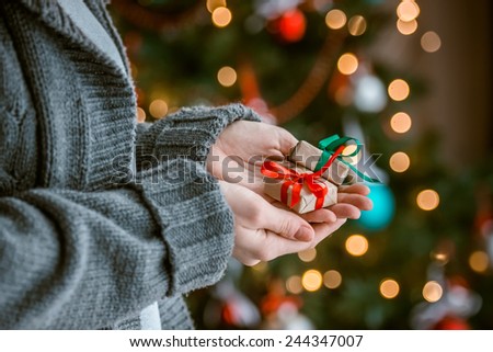 Small gift boxes in woman hands near decorated tree - christmas present, luxury life. Toned picture