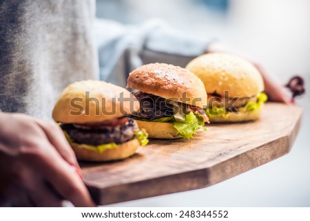 Three delicious hamburgers on wooden board. Toned image