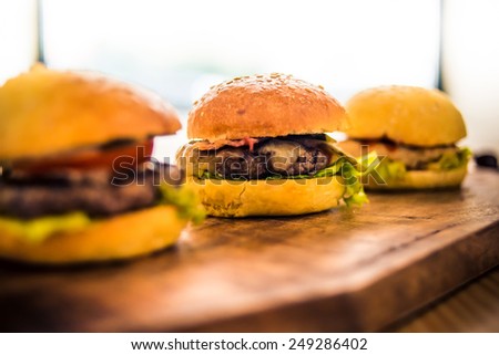 Three delicious hamburgers on wooden board