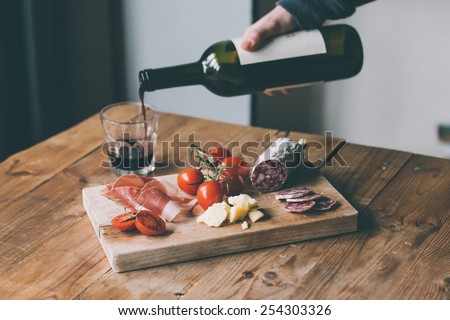 Appetizers - tomato, meat and cheese - on wooden board with bottle of wine and glass. Toned image