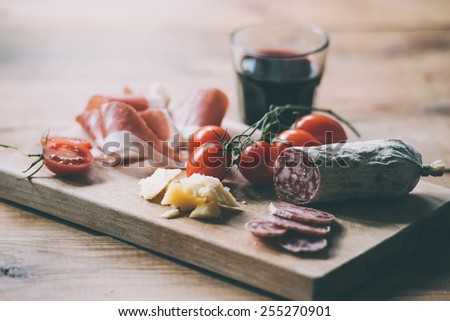 Appetizers - tomato, meat and cheese - on wooden board with  glass of wine. Toned image