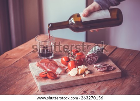 Appetizers - tomato, meat and cheese - on wooden board with bottle of wine and glass. Toned image