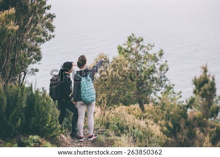 Two girl tourists with backpacks standing on  a mountain, searching the trail. Toned image