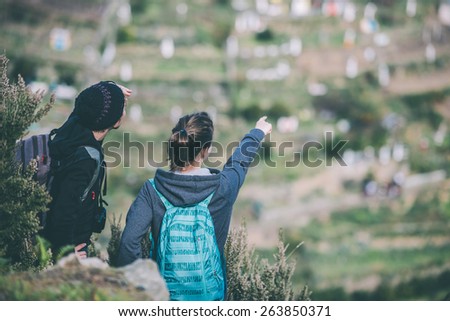 Two girl tourists with backpacks standing on  a mountain, searching the trail. Toned image