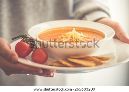 Plate of tomato soup served with cheese and toasts in hands. Toned picture