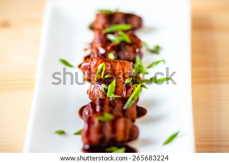 Snack appetizer - dried dates wrapped with bacon and dressed with balsamic creme vinegar and green onions. Selective focus