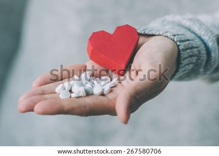 White pills and paper heart in hands. Medicine and health care concept. Toned image