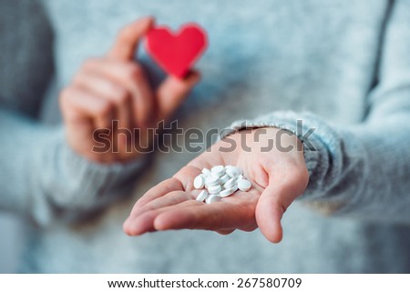 White pills and paper heart in hands. Medicine and health care concept