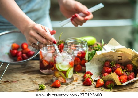 Preparation of lemonade - three retro glass jars, strawberries, cucumber and mint on wooden table