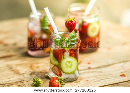 Three retro glass jars of lemonade with  strawberries, cucumber and mint on wooden table