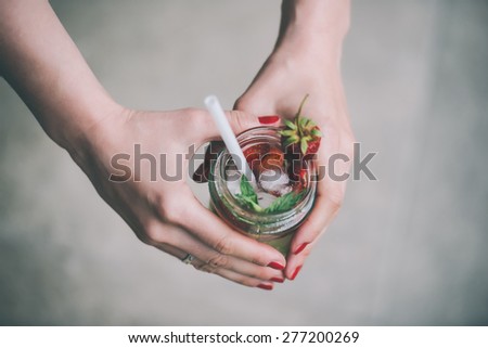Retro glass jar of lemonade with  strawberries, cucumber and mint in hands. Toned image