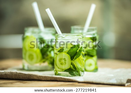 Three retro glass jars of lemonade with cucumber and mint on wooden table