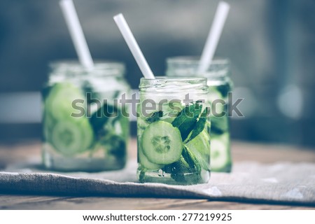 Three retro glass jars of lemonade with cucumber and mint on wooden table. Toned image
