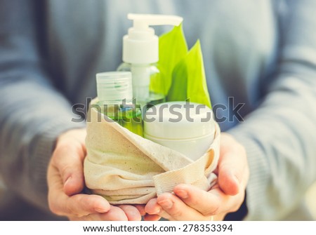 Cosmetic bottle container with green herbal leaves in small organic cotton bag in woman hands. Toned image. Selective focus