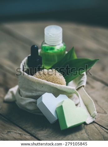 Cosmetic bottle container with green herbal leaves in small organic cotton bag on wooden background. Toned image