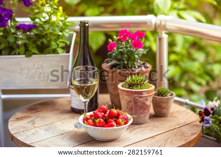 Strawberry, glass of wine and flowers on small wooden table on beautiful terrace or balcony