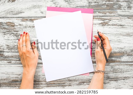 Female hands holding pen and blank paper sheets with copyspace on old wooden table. Top view