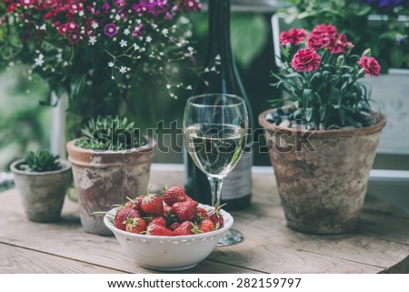 Strawberry, glass of wine and flowers on small wooden table on beautiful terrace or balcony. Toned image
