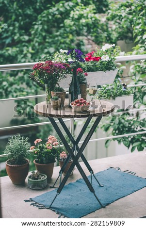 Strawberry, glass of wine and flowers on small wooden table on beautiful terrace or balcony. Toned image