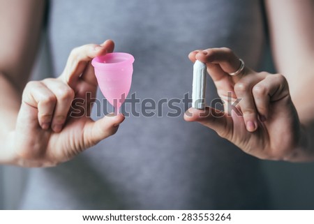 Young woman hands holding different types of feminine hygiene products - menstrual cup and tampons