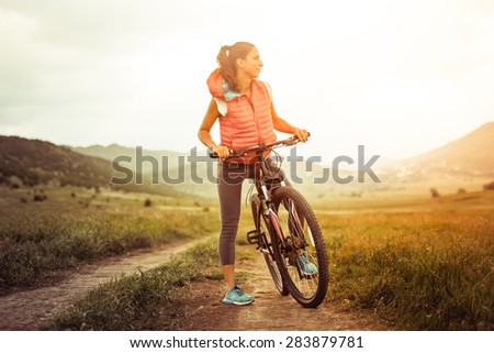 Beautiful girl on riding bicycle outdoor on the rural road. Wellness and sport concept