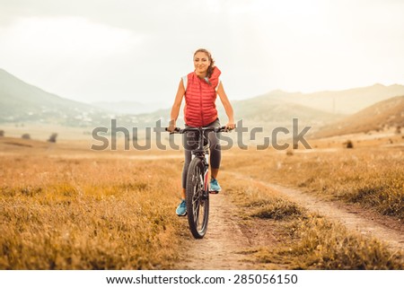 Beautiful girl riding on bicycle outdoor on the rural road. Wellness and sport concept