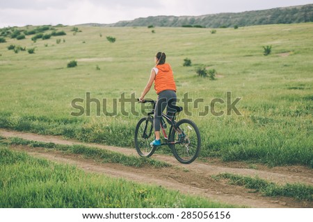 Beautiful girl riding on bicycle outdoor on the rural road. Wellness and sport concept. Toned image