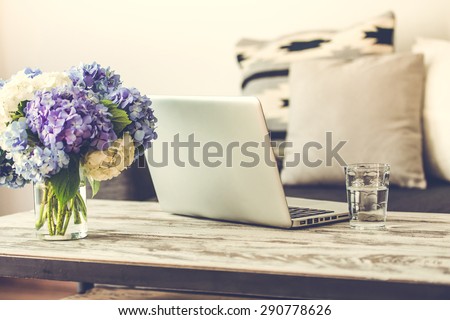 Modern wooden coffee table, laptop and cozy sofa with pillows. Living room interior and home decor concept. Toned image