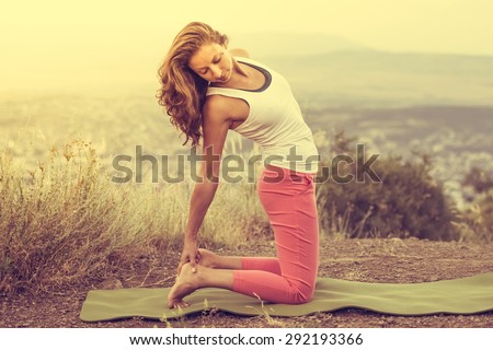 Young woman practicing yoga outdoor in the nature with city on background. Toned image