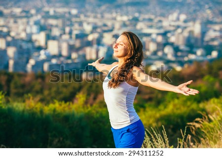 Young woman spreading hands wide open with city on background. Freedom concept. Love and emotions, woman happiness.
