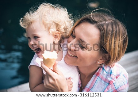 Mother and daughter eat ice-cream during a walk outdoors. Toned image
